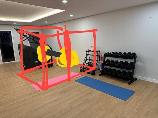 The image depicts a home gym setup with various fitness equipment and a highlighted area for a gym rack.