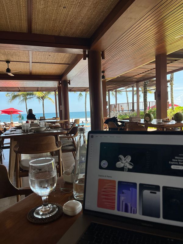 A serene beach club setting with a laptop, water glass, and a view of the ocean.