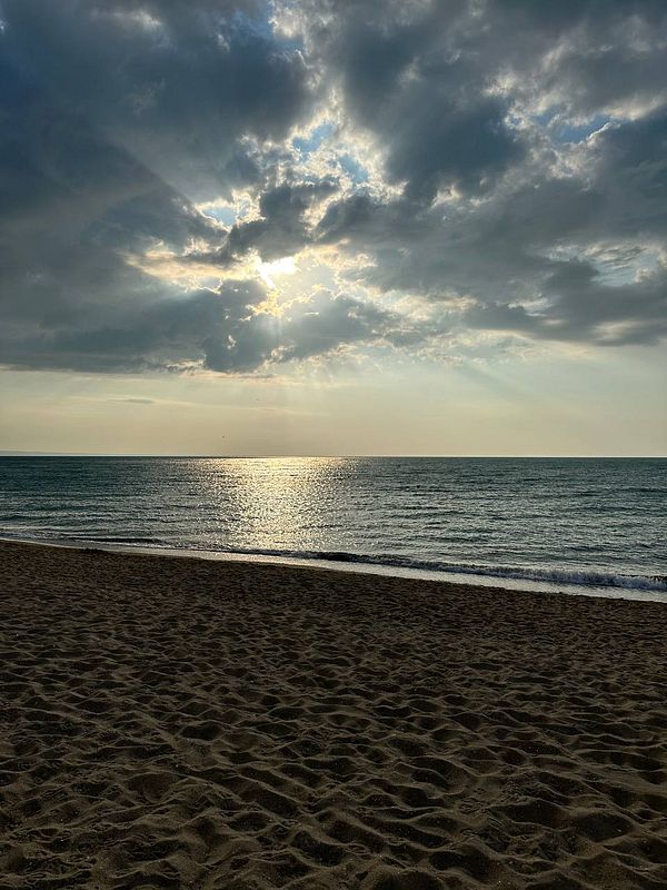 A serene beach scene at sunrise with clouds and gentle waves.