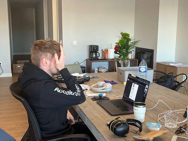A person is sitting at a table, visibly frustrated while working on a laptop in a home office setting.