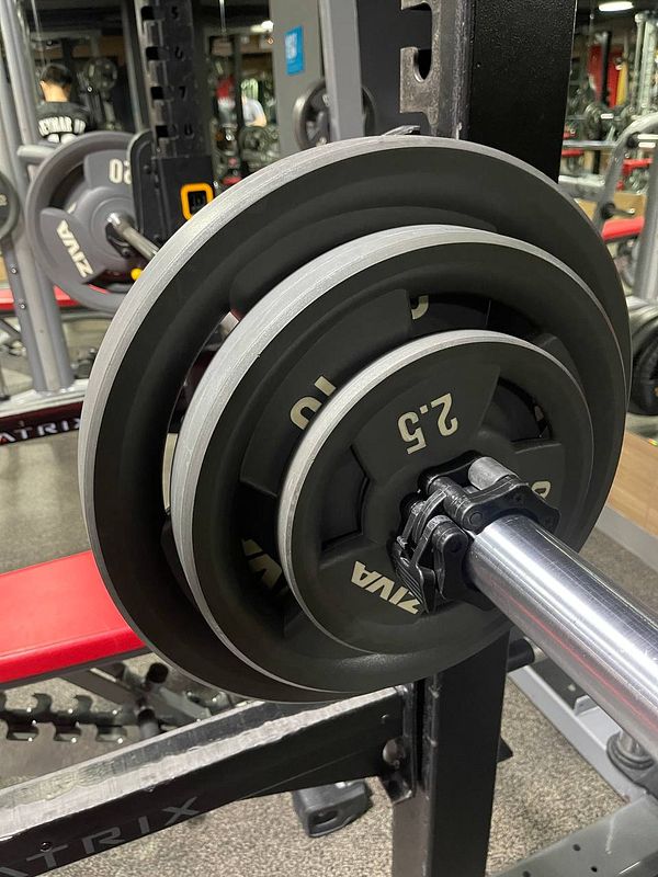 A close-up view of a barbell loaded with weight plates in a gym setting.