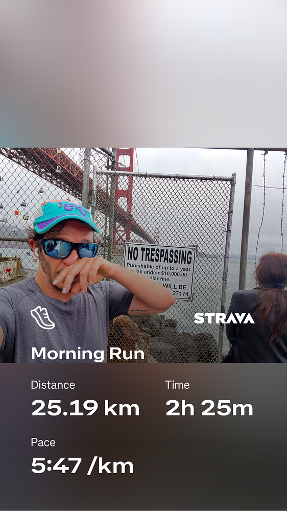 A man takes a selfie on a run beneath the Golden Gate Bridge with running stats overlaid.