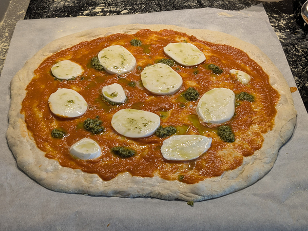 A freshly prepared sourdough pizza topped with tomato sauce, mozzarella, and pesto.