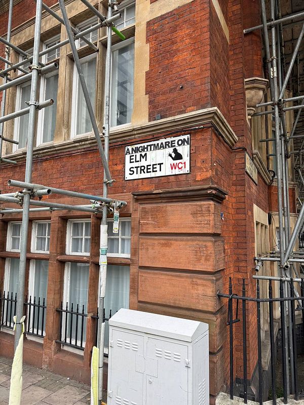 A street sign for 'A Nightmare on Elm Street' is prominently displayed on a building under renovation in London.