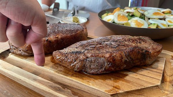A group of six friends enjoys a lively meal with steak and various side dishes at a restaurant table.