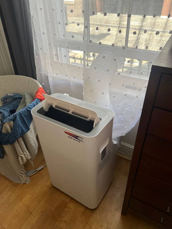 A portable air conditioning unit is set up in a flat, with a vent hose extending through a window.
