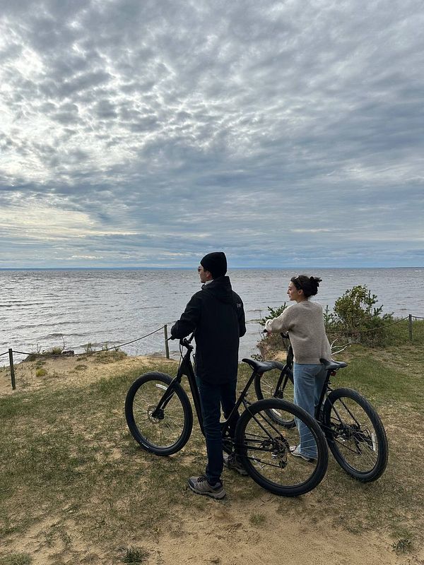 A couple stands by the water, enjoying a scenic view while resting their bikes.