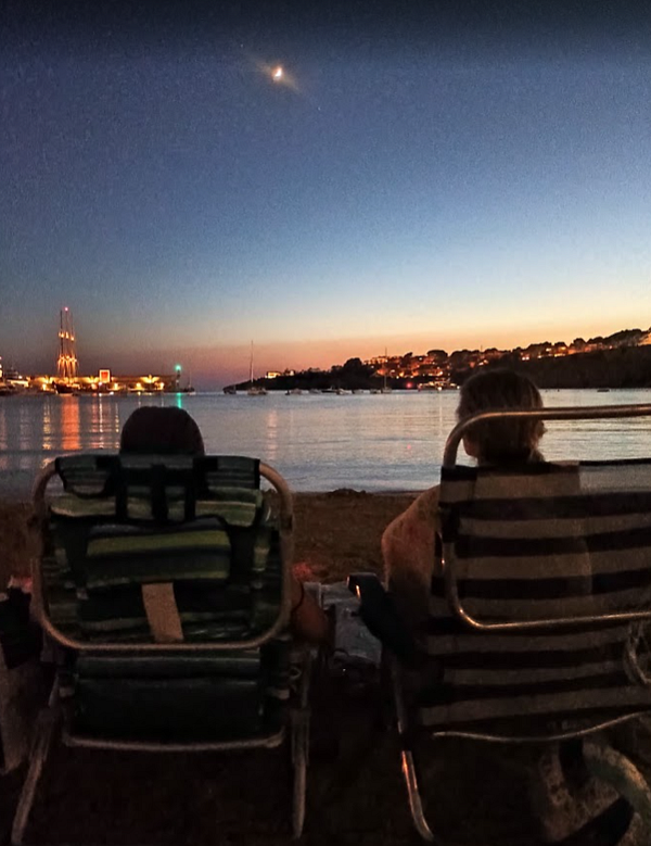 A serene beach scene at dusk featuring two people relaxing in beach chairs.