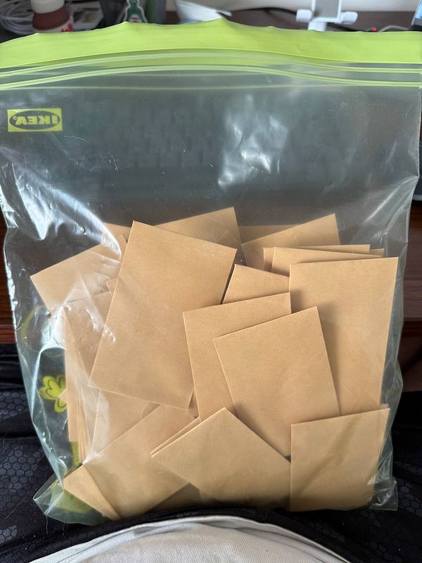 A clear plastic bag filled with small brown envelopes is resting on a person's lap.