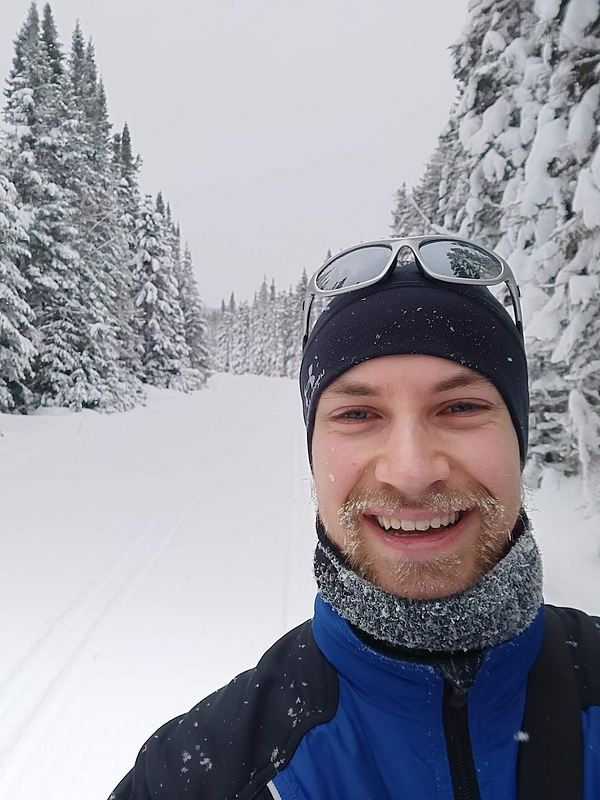 A smiling person stands in a snowy landscape, ready for cross-country skiing.