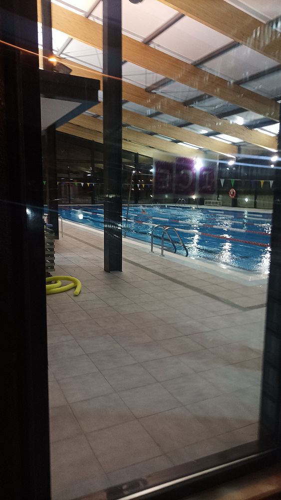 An indoor swimming pool is visible at night, featuring illuminated water and a modern architectural design.