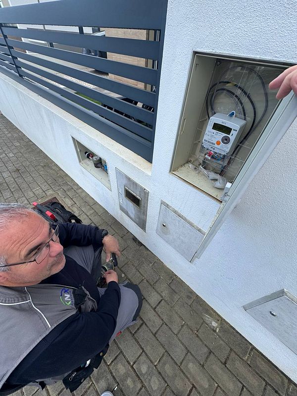 A technician is inspecting an electricity counter installation outside a building.