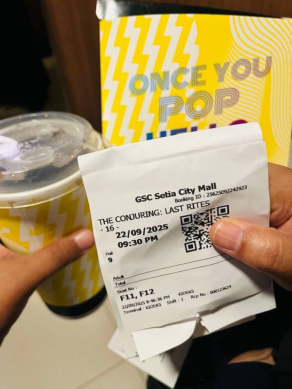 A movie ticket for 'The Conjuring: Last Rites' is held alongside a drink and popcorn bag.