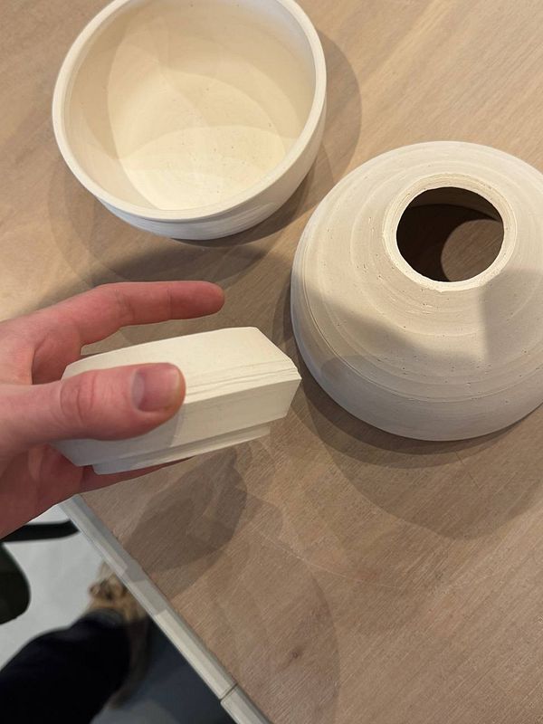 A close-up photograph of pottery pieces glazed in various shades of green and brown, featuring different shapes and designs.