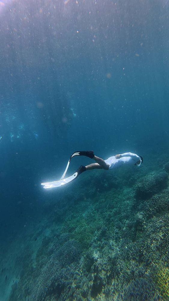 A freediver underwater surrounded by bubbles and light filtering through the water surface.