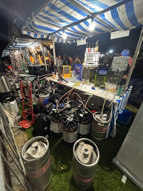 A bustling beer festival booth featuring various kegs and craft beer signage.