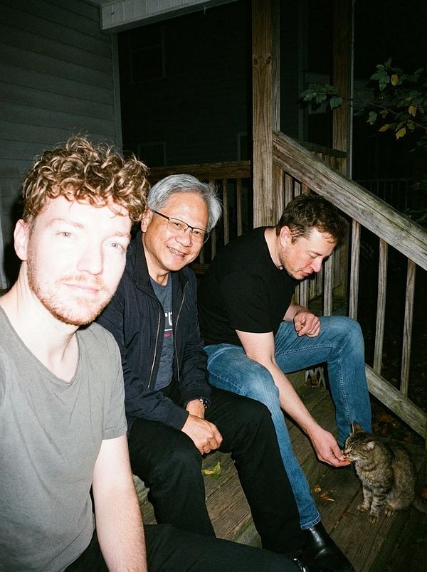 A group of three men and a cat are sitting on a wooden porch at night.