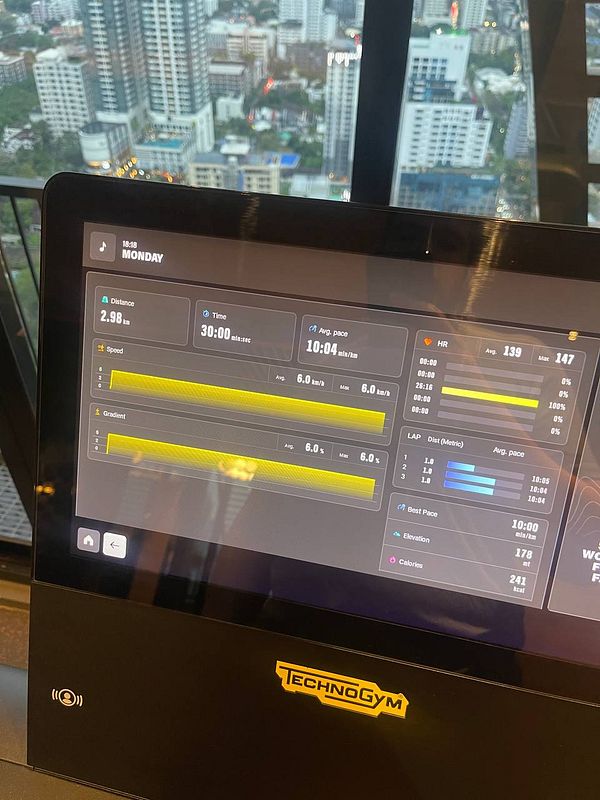 The image displays a fitness machine interface showing workout statistics against a city skyline backdrop.