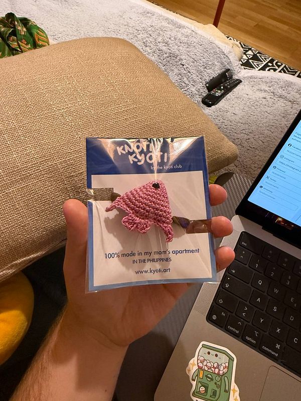 A hand holds a packaging card featuring a crocheted pink animal hairband.