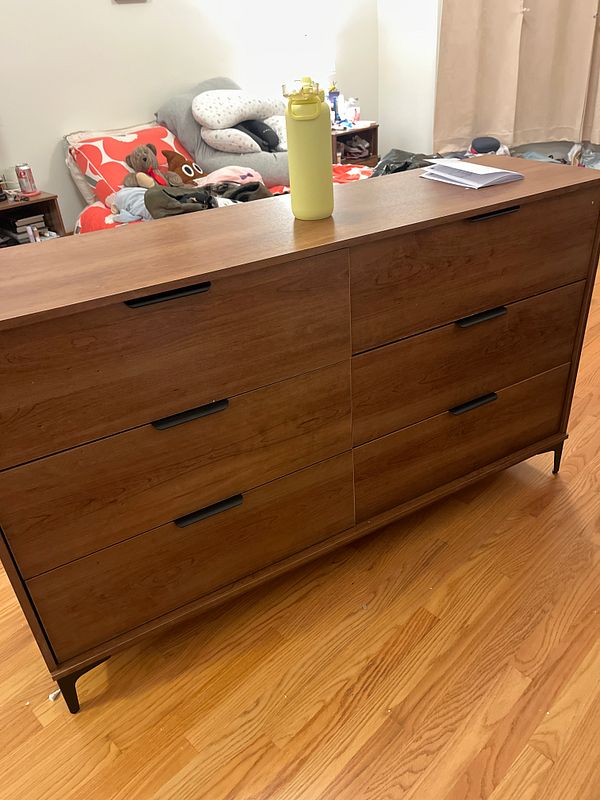 Photo of a partially assembled wooden dresser frame on a carpeted floor with tools and components nearby.