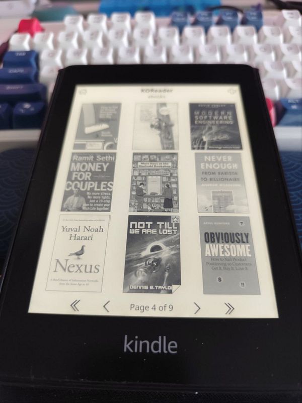 A Kindle Paperwhite displays a selection of book covers on its screen.