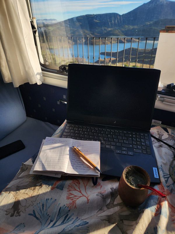 A cozy workspace featuring a laptop, a notebook, and a traditional mate cup with a scenic view in the background.