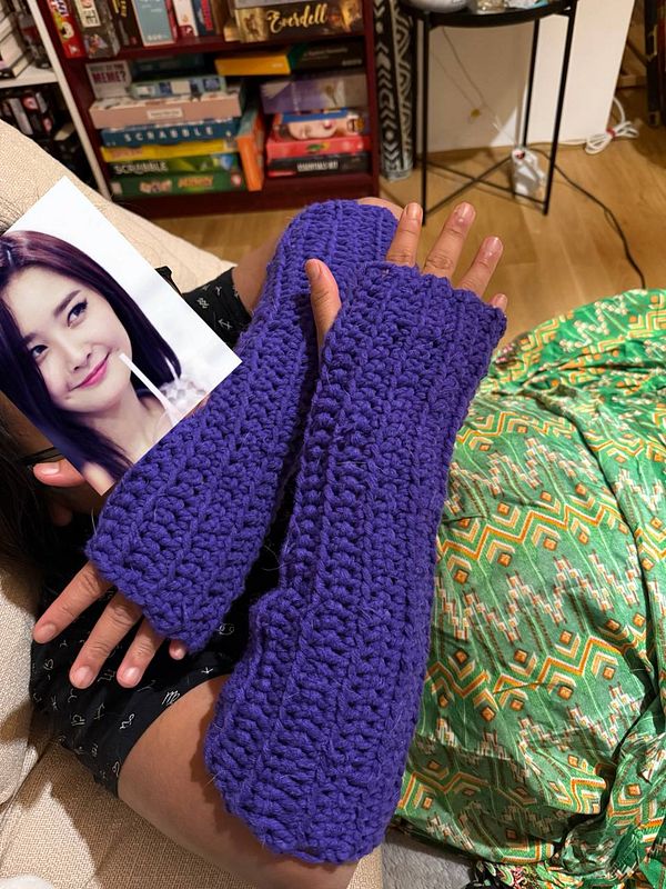 A person is wearing handmade purple crocheted hand warmers while holding a photo of a woman.
