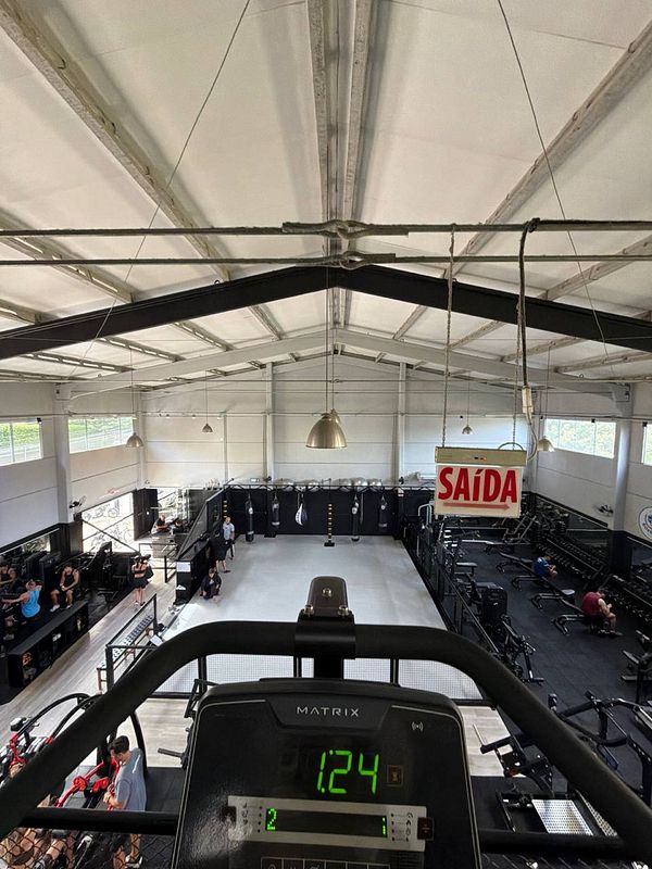 A young man lifting weights in a gym with a dumbbell in each hand, standing in front of gym equipment and mirrors.