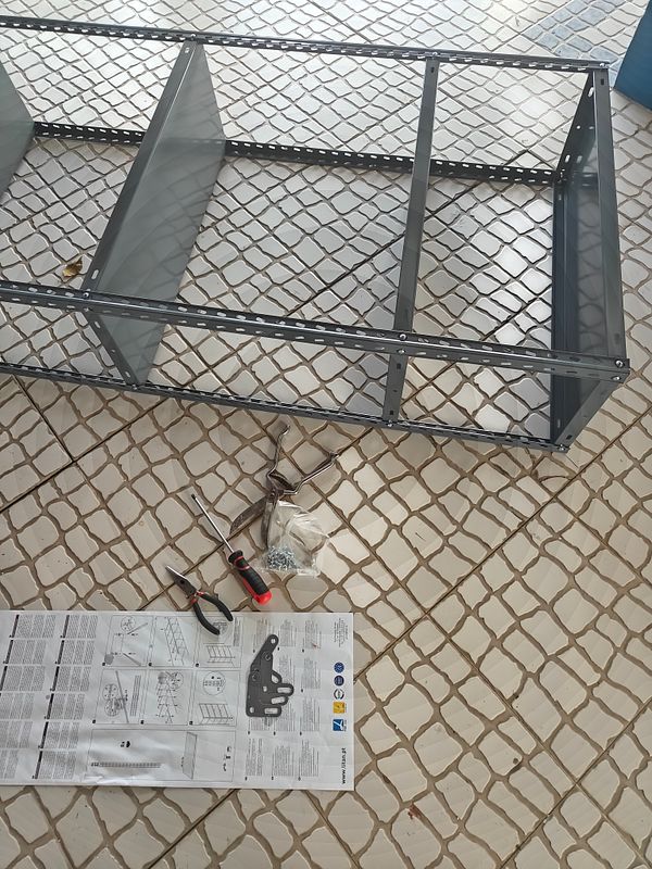 An assembly project is underway with metal parts and tools laid out on a tiled surface.