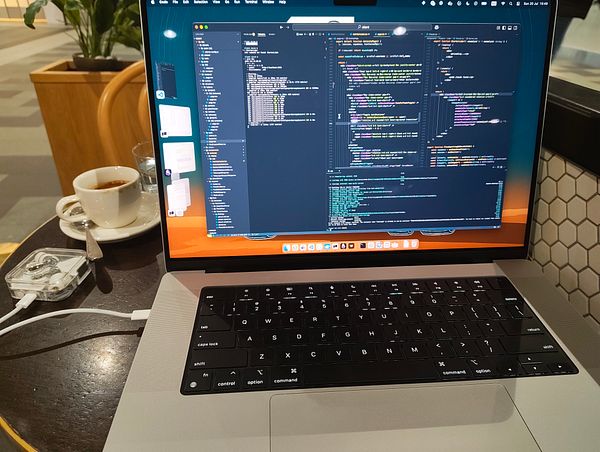 A laptop displaying code is set on a table next to a cup of coffee in a cafe.