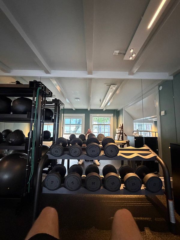 A person wearing athletic clothing is exercising on an elliptical machine in a gym setting with industrial elements and colorful lighting.