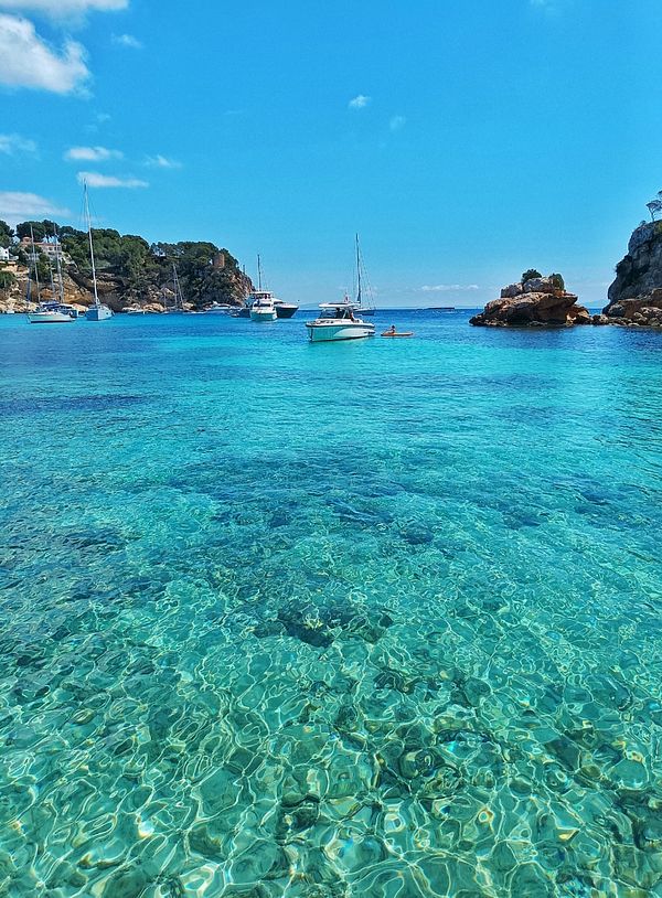 A picturesque beach scene featuring clear turquoise waters and boats anchored in a serene bay.