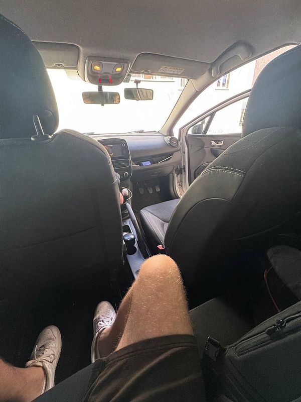 The image captures the interior of a car from the back seat perspective, focusing on the front dashboard and the driver's seat.