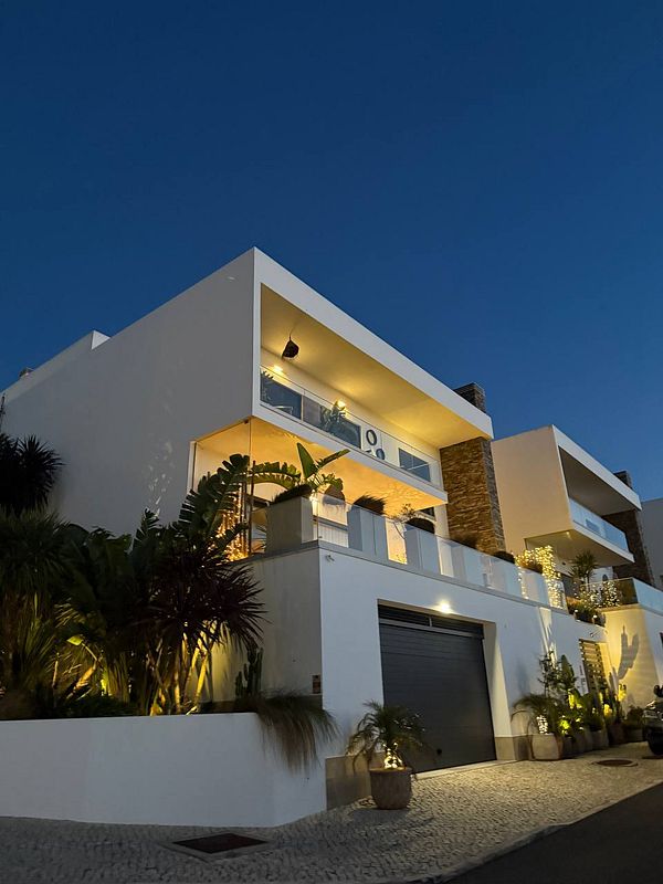 A modern, well-lit house with a sleek design and lush greenery in the foreground.