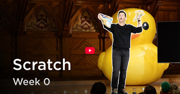 A presenter stands in front of a large inflatable rubber duck while discussing Scratch programming in a lecture setting.