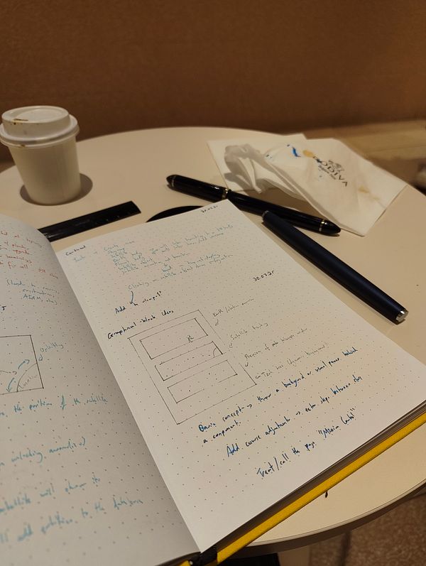 A workspace featuring a notebook filled with handwritten notes, fountain pens, and a coffee cup.