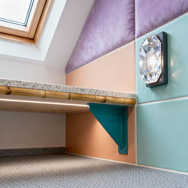 A close-up of a contemporary kids’ room corner under a sloped ceiling with a wood-framed skylight. Large pastel tiles in mint and blush line the wall with a plush lavender panel above; a faceted crystal sconce is mounted on the mint tile. A narrow shelf with a speckled terrazzo top and rounded bamboo edge is supported by a teal metal bracket and lit by an integrated LED strip beneath. The floor is speckled gray, creating a clean, playful setting.