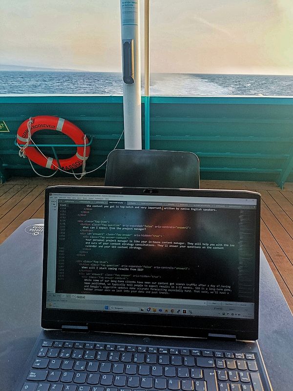 A laptop displaying code is set on a table aboard a ferry with a view of the ocean.