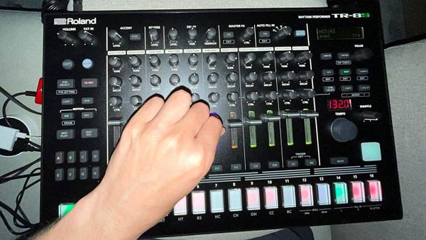 A hand is adjusting the controls on a Roland TR-8S drum machine.
