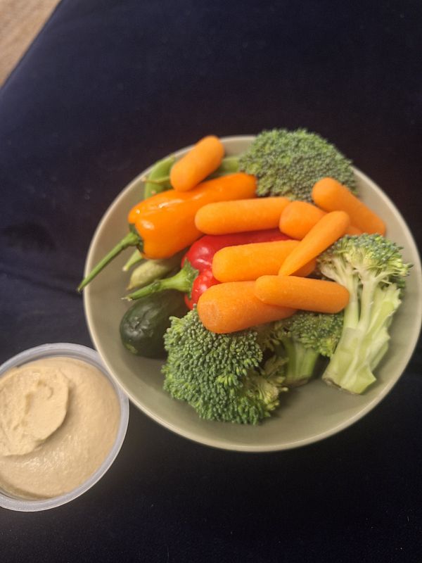 A bowl filled with a variety of fresh vegetables and a side of hummus.