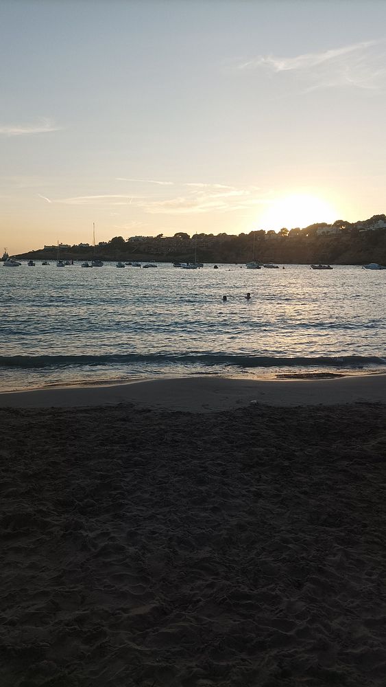 A serene beach scene at sunset with swimmers in the water.