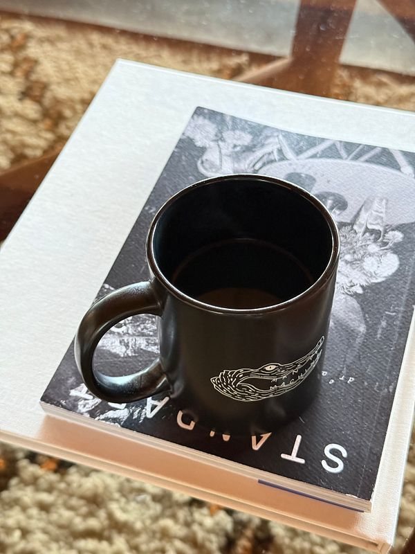 A black coffee mug rests on top of a book on a table.
