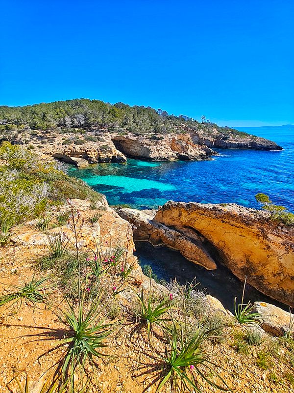 A scenic mountain landscape with a person hiking beside a calm lake and autumn-colored trees under a partly cloudy sky.