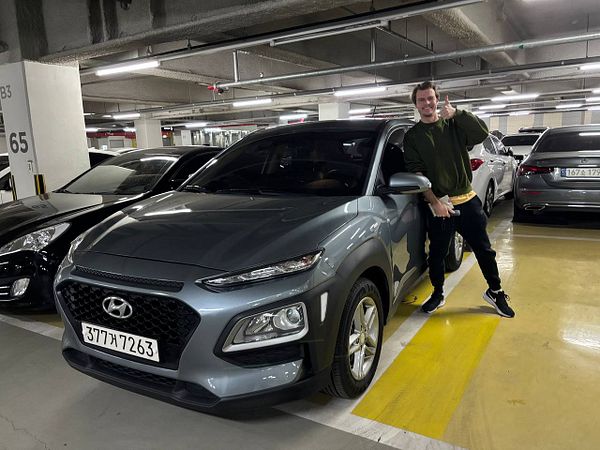 A man stands next to a gray Hyundai Kona in a parking garage, giving a thumbs-up gesture.
