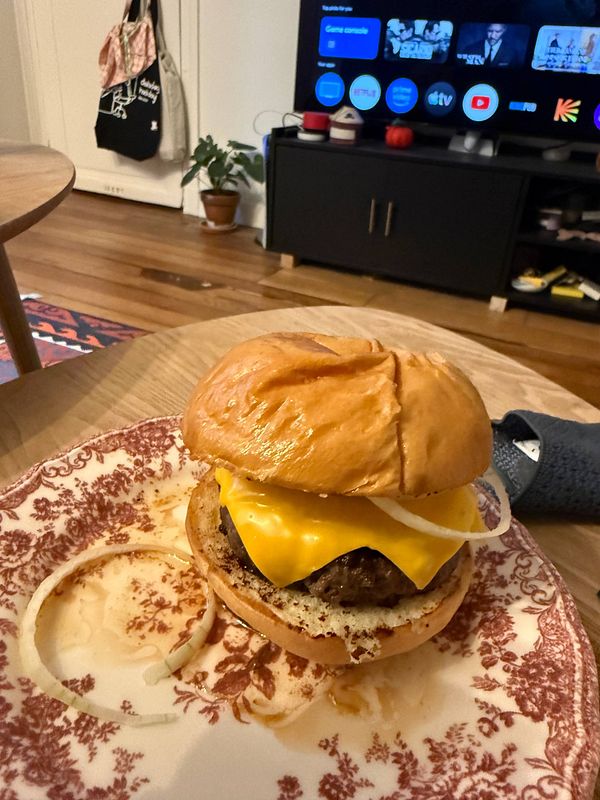 A close-up photo of a hamburger with lettuce, tomato, cheese, and a beef patty inside a sesame seed bun on a white plate.