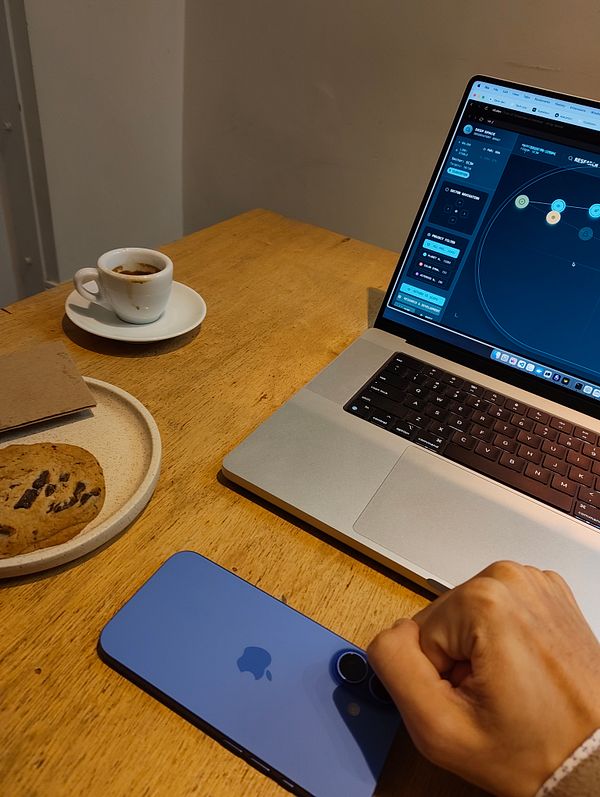 A workspace setup featuring a laptop, a smartphone, a coffee, and a cookie on a wooden table.