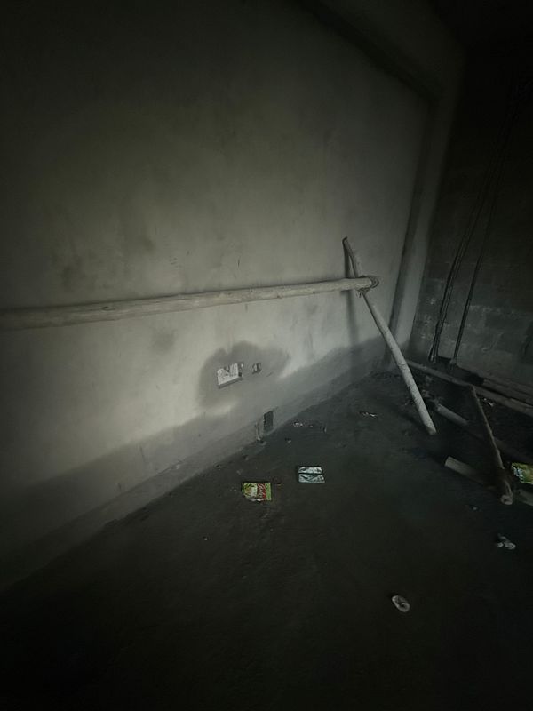 The image depicts an unfinished interior space with a bare wall and scattered debris.