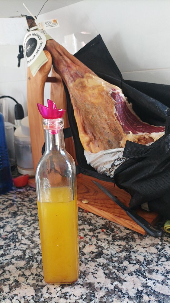 A bottle of homemade olive oil is prominently displayed alongside a hanging piece of cured ham.
