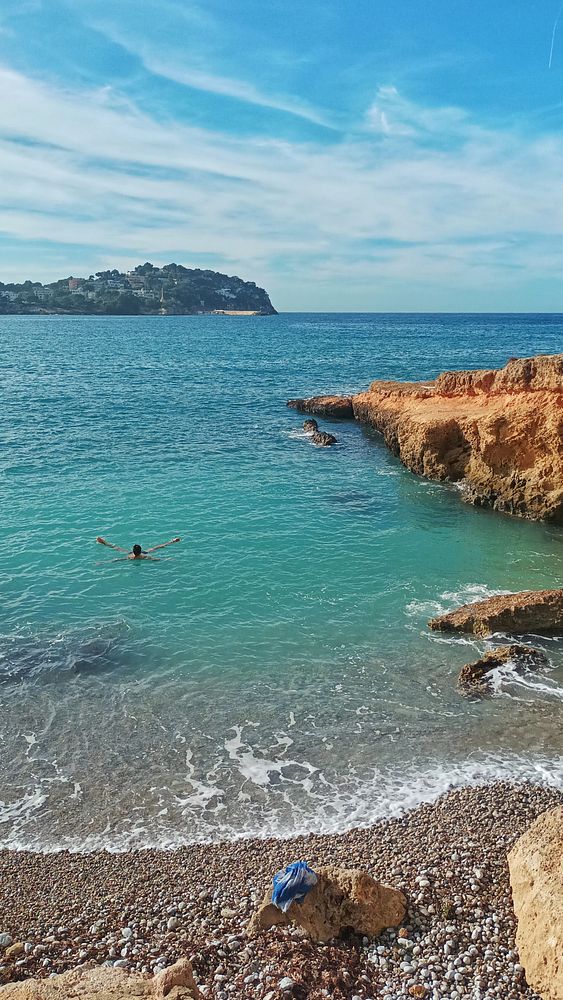 A person is enjoying the water at a scenic beach with rocky formations and a distant island.