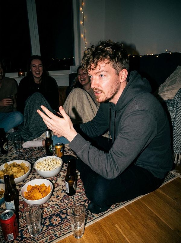 A group of friends enjoys a cozy gathering with snacks and drinks in a warmly lit living room.